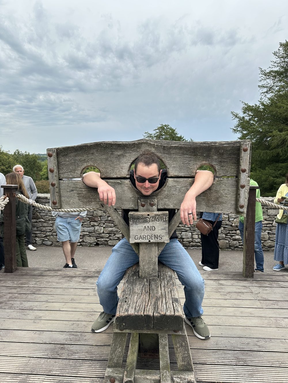 Michael grinning with his head and hands in the wooden stocks at Blarney Castle