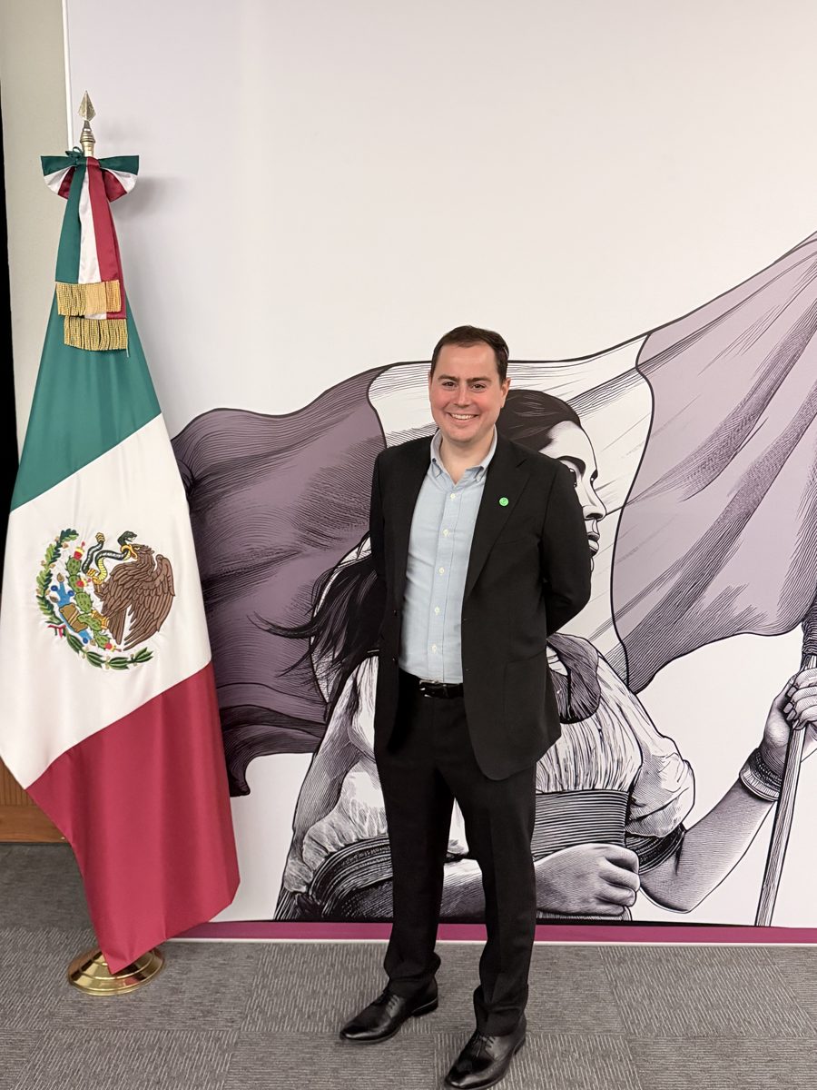 Michael smiling beside the Mexican flag during a government-hosted trip for film producers